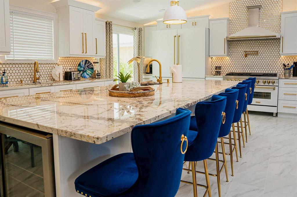 A kitchen features a large marble island with blue velvet stools and gold hardware — 328 6TH AVENUE, INDIAN ROCKS BEACH, FL