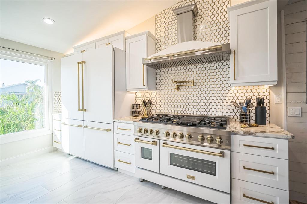 A white kitchen features a ZLINE range, gold hardware, and a hexagonal tile backsplash — 328 6TH AVENUE, INDIAN ROCKS BEACH, FL
