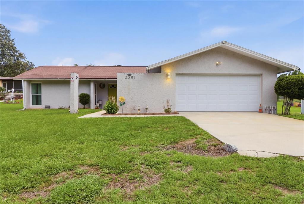 A single-story house with a white stucco exterior, a two-car garage, and a front lawn — 2507 BLUEGRASS STREET, INVERNESS, FL