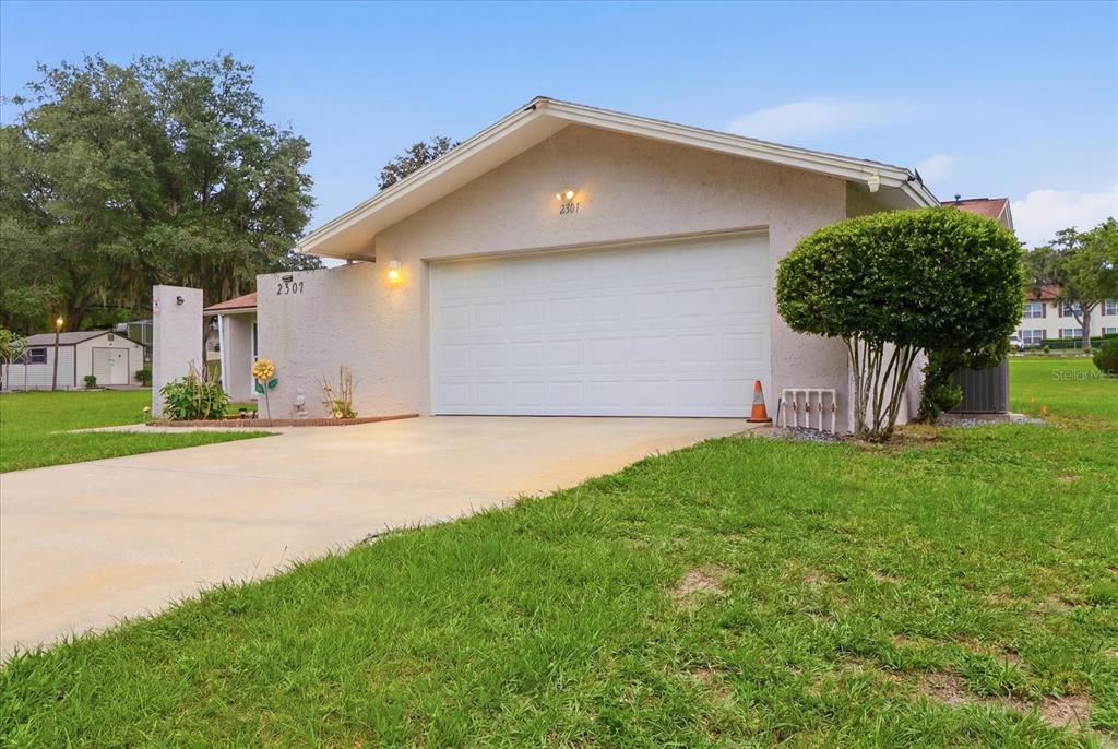 A single-story house exterior features a white garage door, a concrete driveway, and green lawn — 2507 BLUEGRASS STREET, INVERNESS, FL