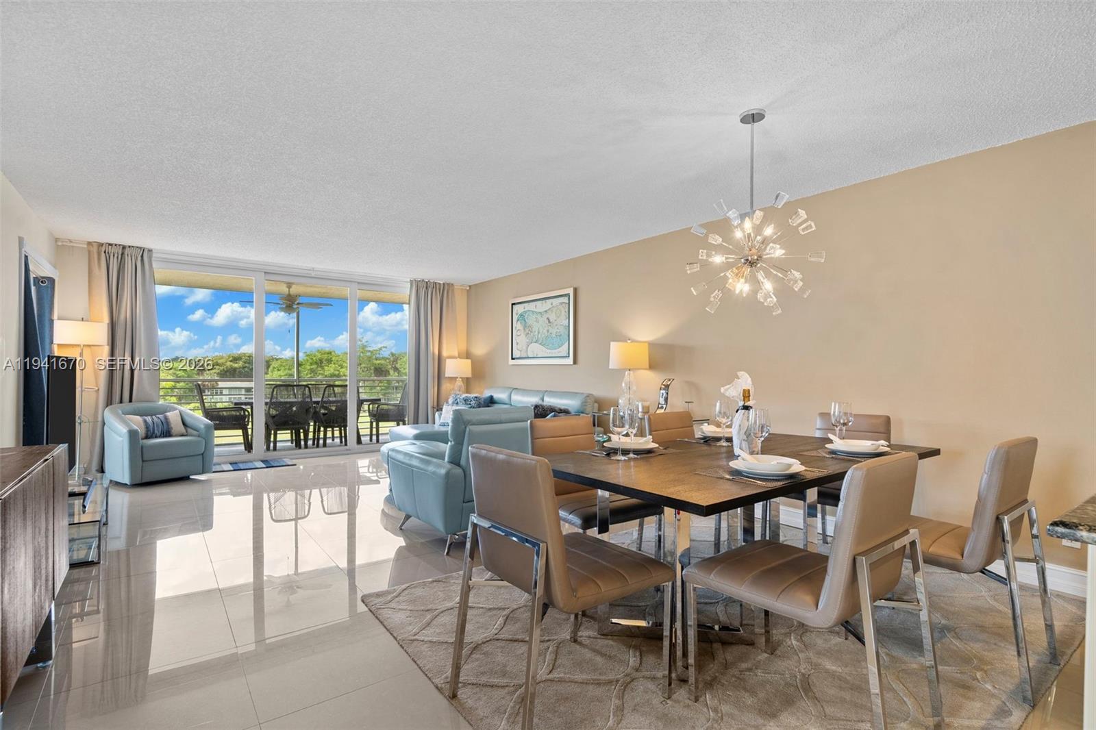 A dining area and living room feature tile floors, a modern chandelier, and balcony access — 4030 W Palm Aire Dr # 408, Pompano Beach FL 33069, POMPANO BEACH, FL