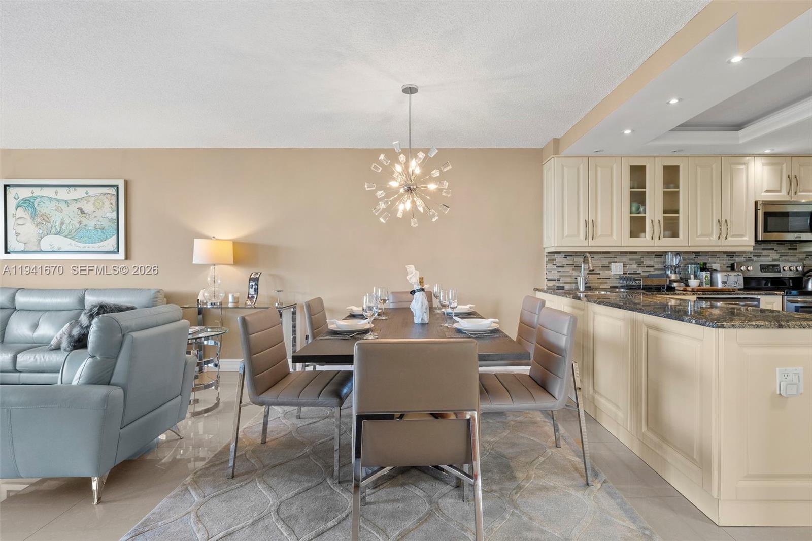 A dining area features a modern chandelier, a dark table, and light-colored kitchen cabinetry — 4030 W Palm Aire Dr # 408, Pompano Beach FL 33069, POMPANO BEACH, FL