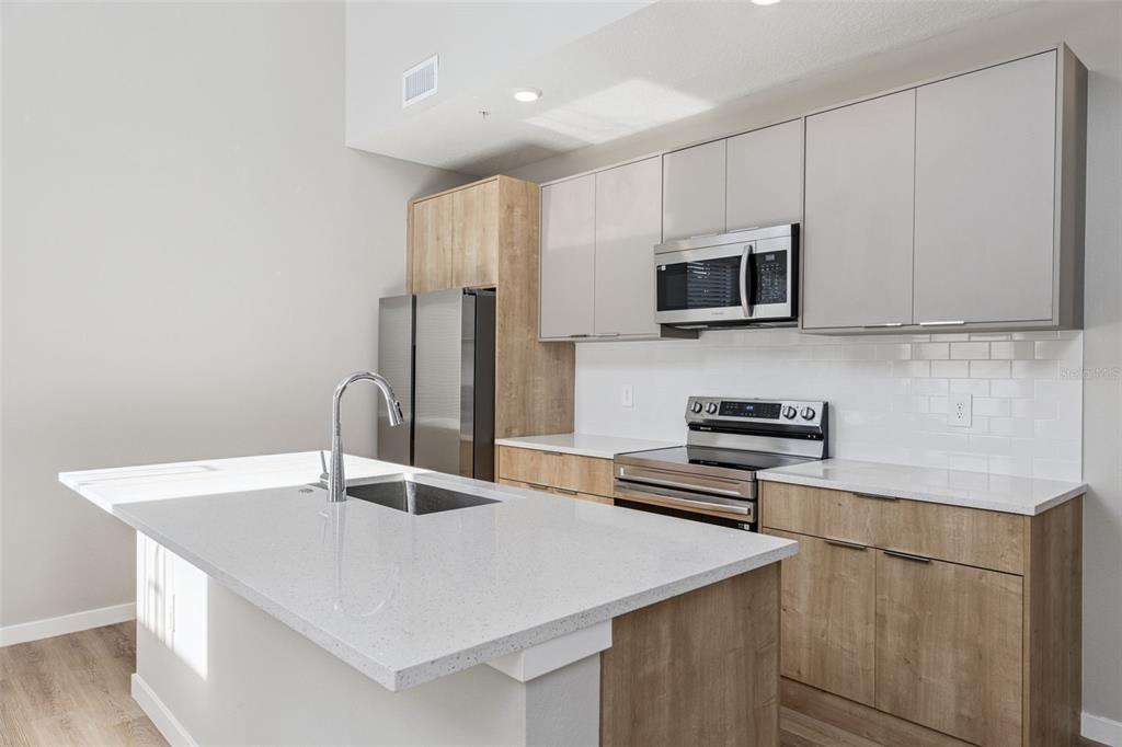 A modern kitchen features a white quartz island, wood-tone lower cabinets, and light gray upper cabinets — 544 N BUMBY AVENUE UNIT 5, ORLANDO, FL