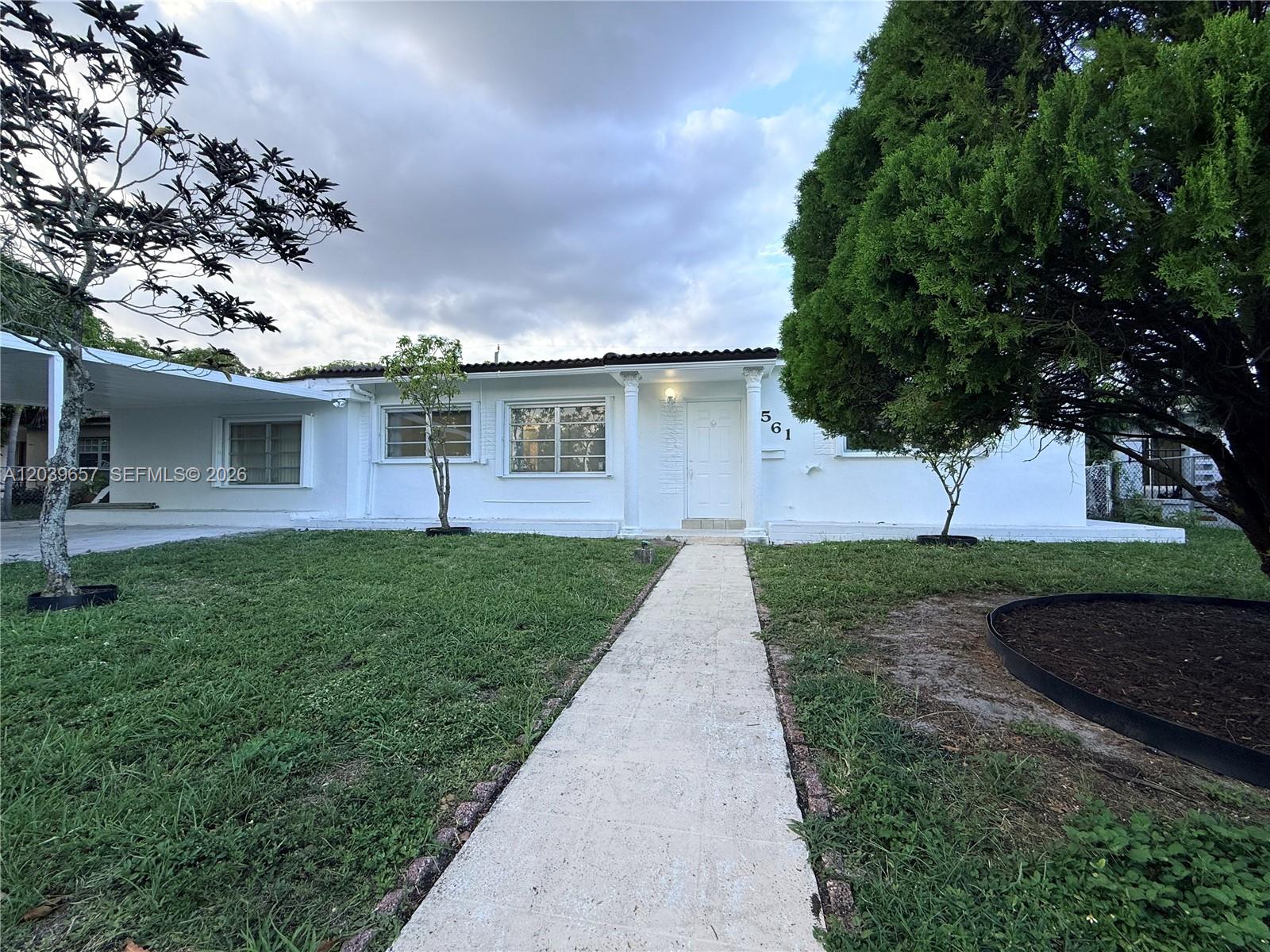 A white single-story house features a front walkway, a carport, and mature landscaping — 561 W 39th St, Hialeah FL 33012, HIALEAH, FL