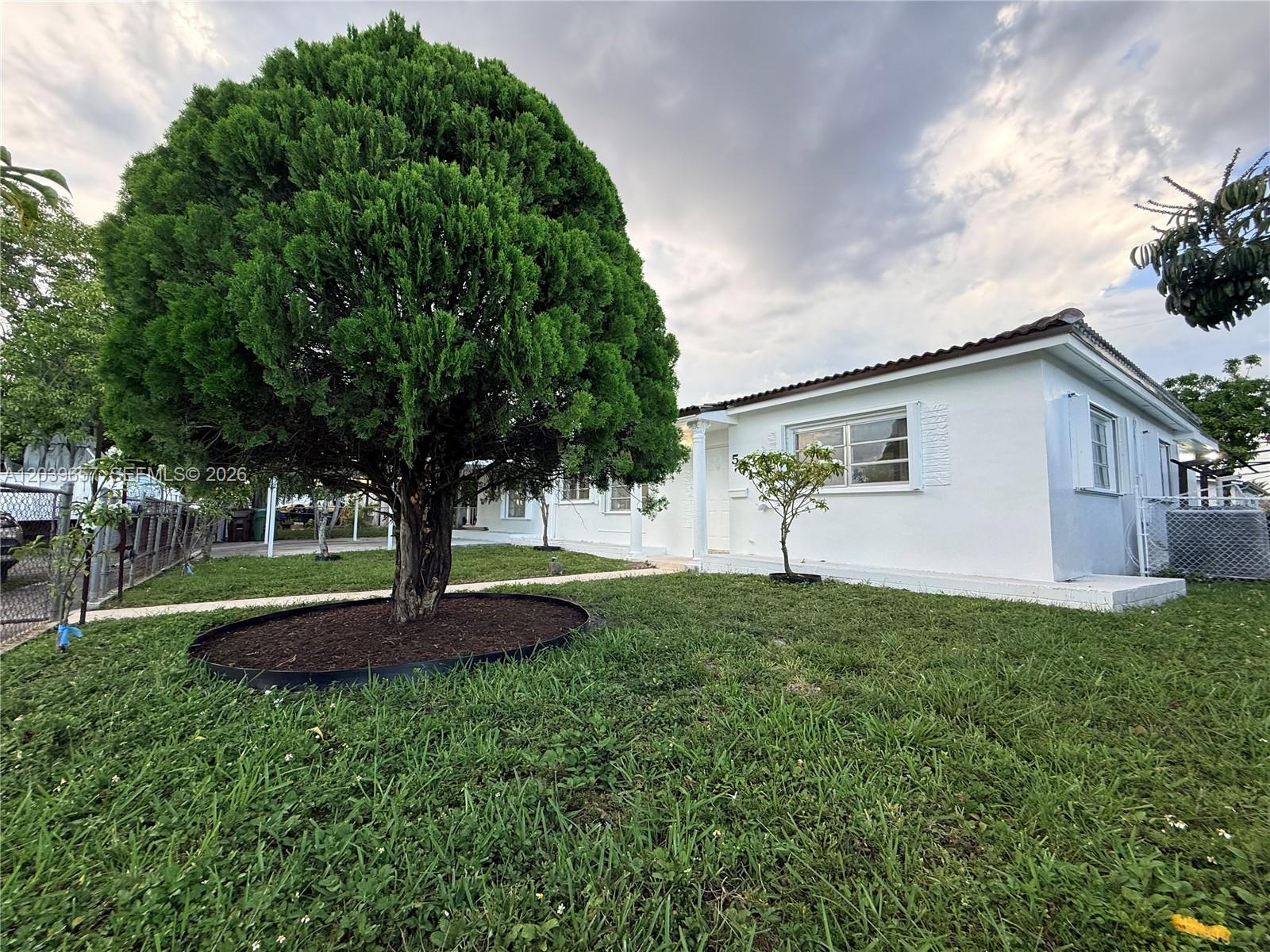 A white single-story house features a large evergreen tree in the front yard — 561 W 39th St, Hialeah FL 33012, HIALEAH, FL