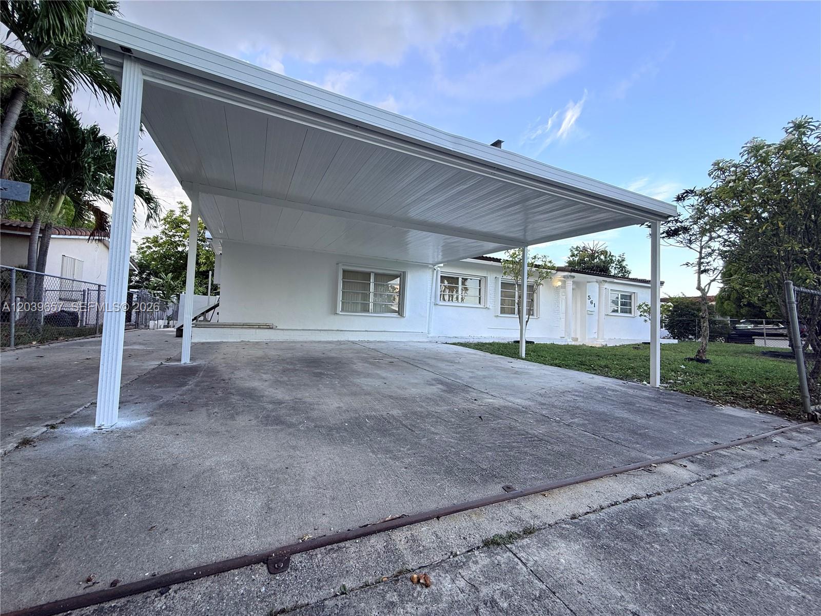 A white single-story house features a large metal carport covering a concrete driveway — 561 W 39th St, Hialeah FL 33012, HIALEAH, FL