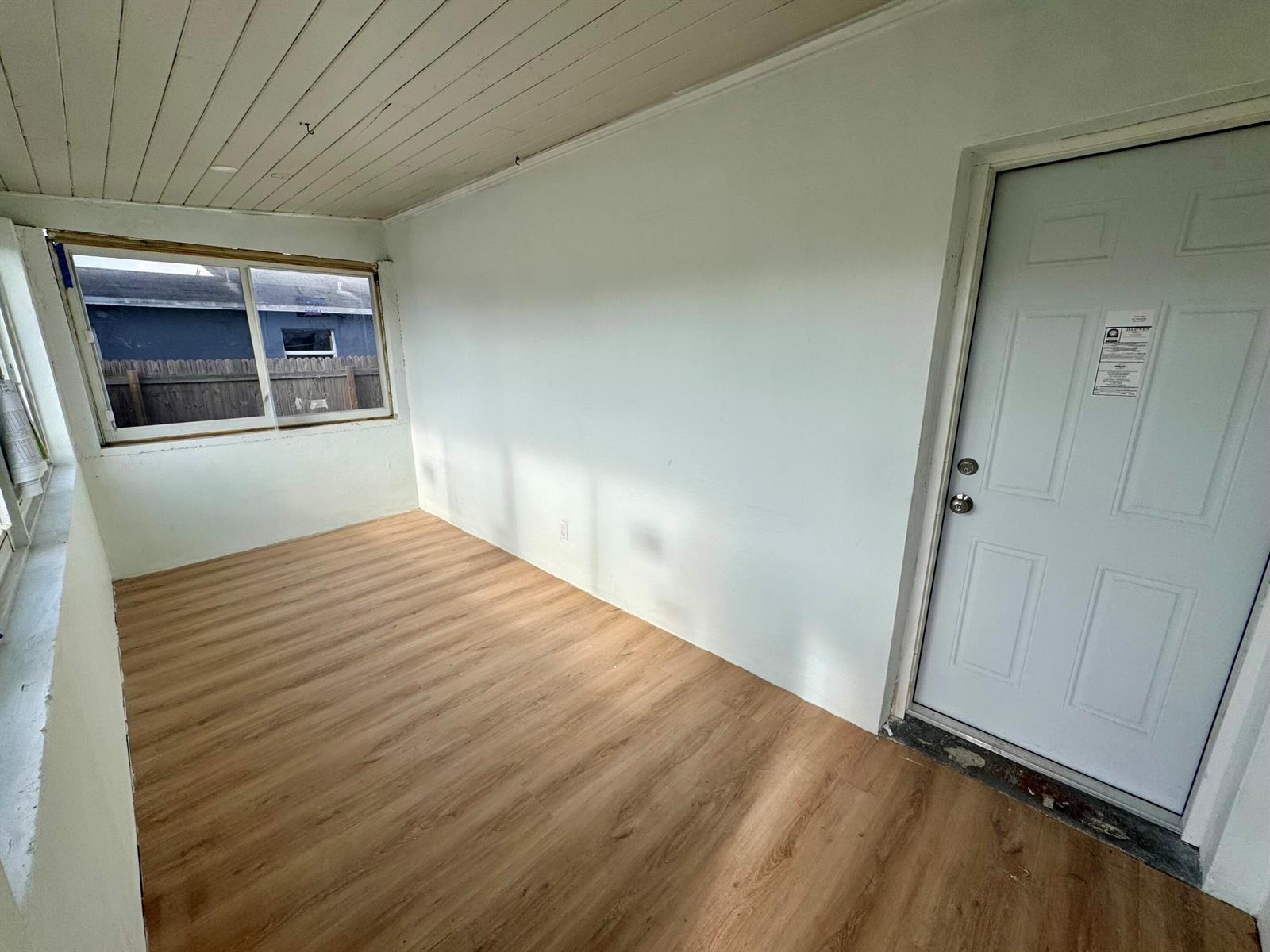 A sunroom features light wood-look flooring, white walls, a ceiling with exposed beams, and a door — 2513 Avenue E, Riviera Beach FL 33404, RIVIERA BEACH, FL