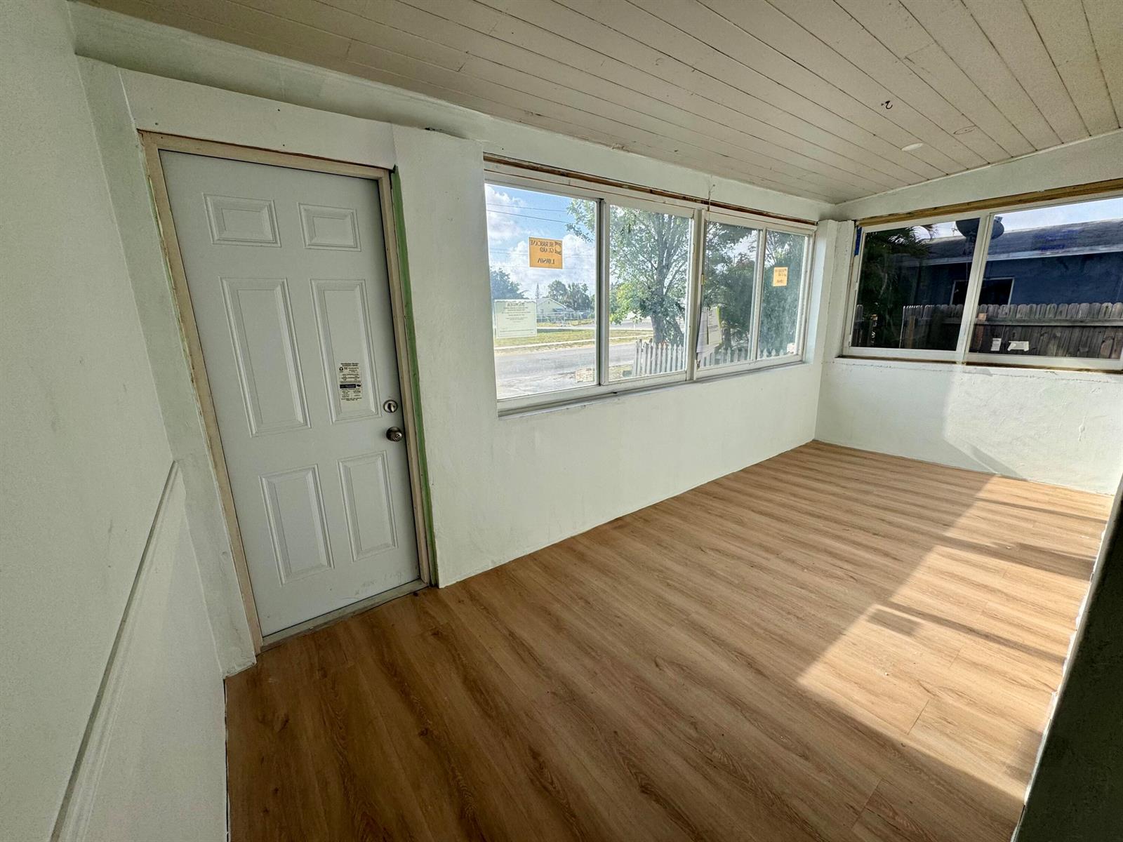 A sunroom with white walls, wood-look flooring, a white door, and multiple large windows — 2513 Avenue E, Riviera Beach FL 33404, RIVIERA BEACH, FL