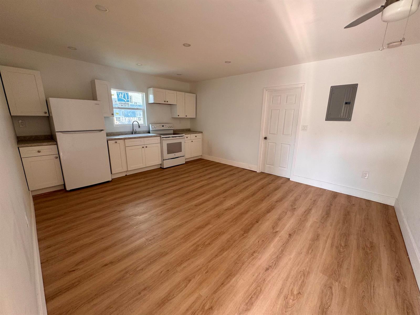A kitchen with white cabinets, stainless steel appliances, and wood-look flooring in an open room — 2513 Avenue E, Riviera Beach FL 33404, RIVIERA BEACH, FL