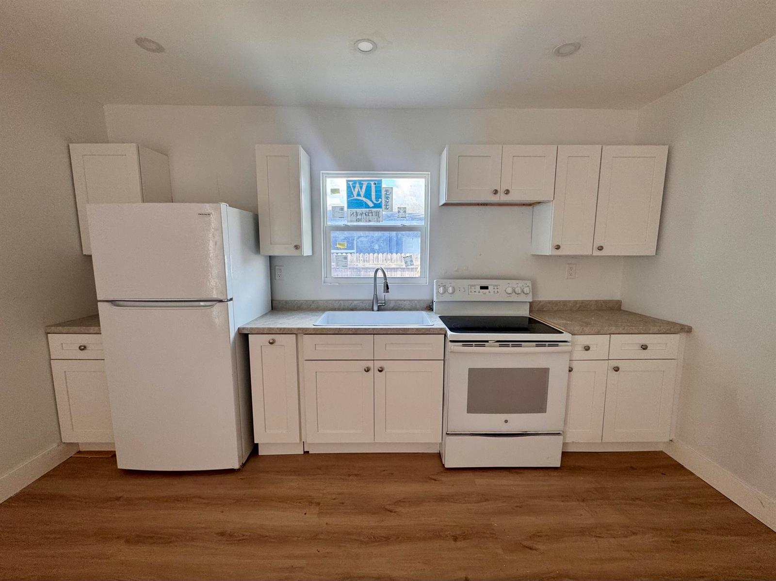 A kitchen features white cabinets, white appliances, a window above the sink, and wood-look flooring — 2513 Avenue E, Riviera Beach FL 33404, RIVIERA BEACH, FL