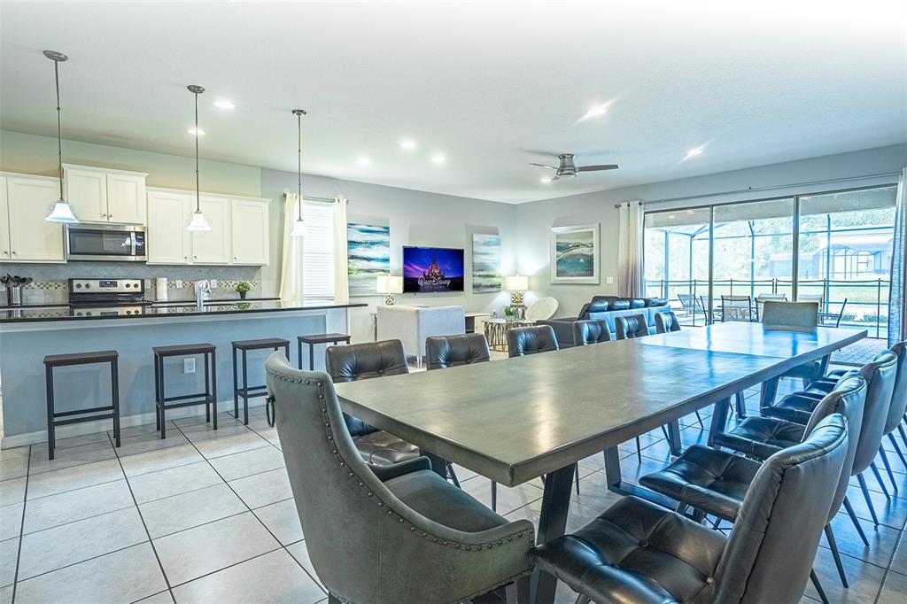 An open-concept kitchen and dining area features a long table, bar seating, and tile flooring — 1682 LIMA AVENUE, KISSIMMEE, FL