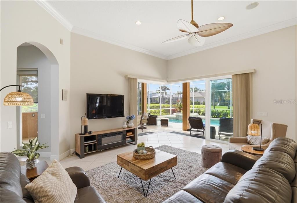 A living room features a television, wooden coffee table, and sliding doors opening to a pool — 8843 17TH AVENUE CIRCLE NW, BRADENTON, FL