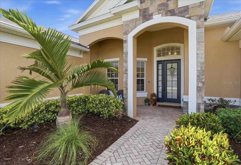 A paved walkway leads to the front entrance of a house with stone-accented columns — 8843 17TH AVENUE CIRCLE NW, BRADENTON, FL