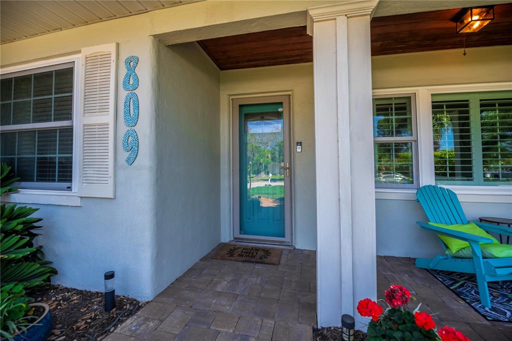 A covered front porch features a teal storm door, blue house numbers, and a chair — 809 NOKOMIS AVENUE S, VENICE, FL