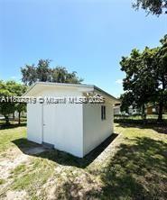 A small, white, detached storage shed stands in a grassy yard under a clear sky — 2740 NW 49th St, Miami FL 33142, MIAMI, FL