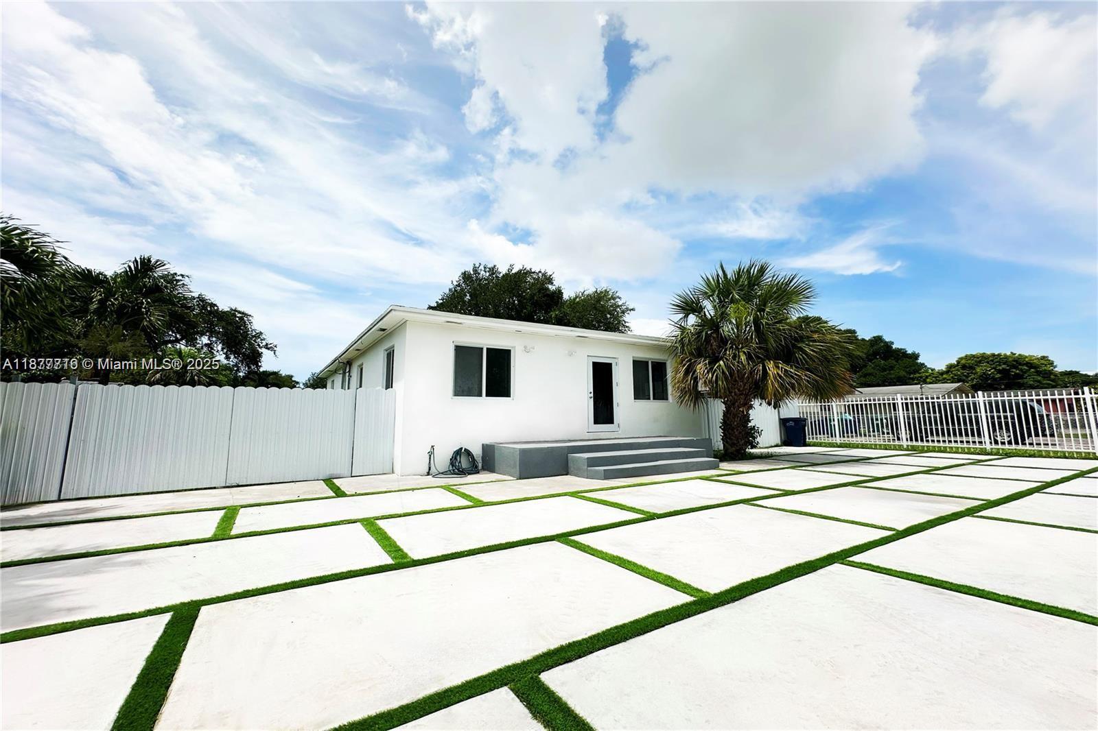 The exterior of a white house features a concrete paver patio with artificial grass strips — 2740 NW 49th St, Miami FL 33142, MIAMI, FL