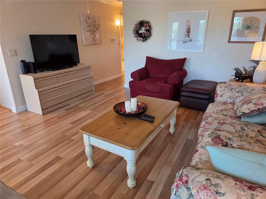A living room features wood-look flooring, a floral sofa, a red armchair, and a coffee table — 11225 82ND AVENUE UNIT 309, SEMINOLE, FL