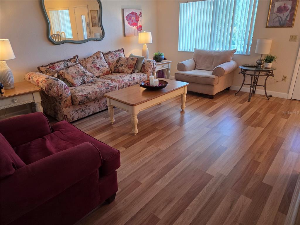 A living room features floral and solid-colored furniture, a wooden coffee table, and wood flooring — 11225 82ND AVENUE UNIT 309, SEMINOLE, FL