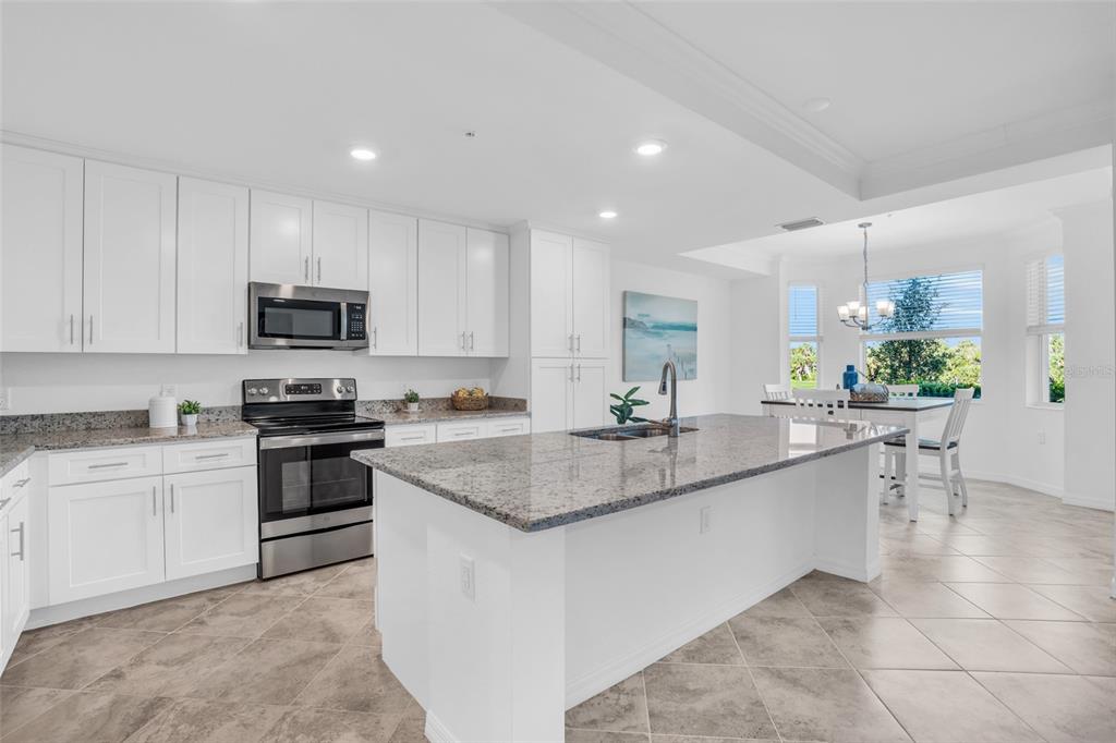 A bright kitchen features white cabinets, granite countertops, a central island, and a dining area — 14041 HERITAGE LANDING BOULEVARD UNIT 616, PUNTA GORDA, FL