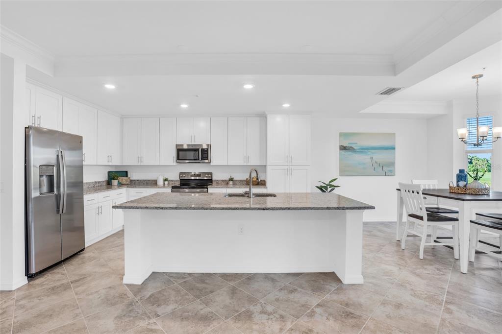 A bright kitchen features white cabinetry, granite countertops, a central island, and tile flooring — 14041 HERITAGE LANDING BOULEVARD UNIT 616, PUNTA GORDA, FL