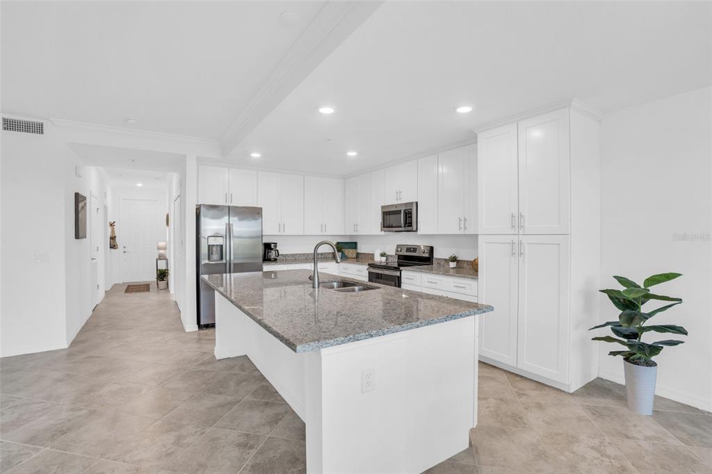 A modern kitchen features white cabinetry, granite countertops, a central island, and tile flooring — 14041 HERITAGE LANDING BOULEVARD UNIT 616, PUNTA GORDA, FL