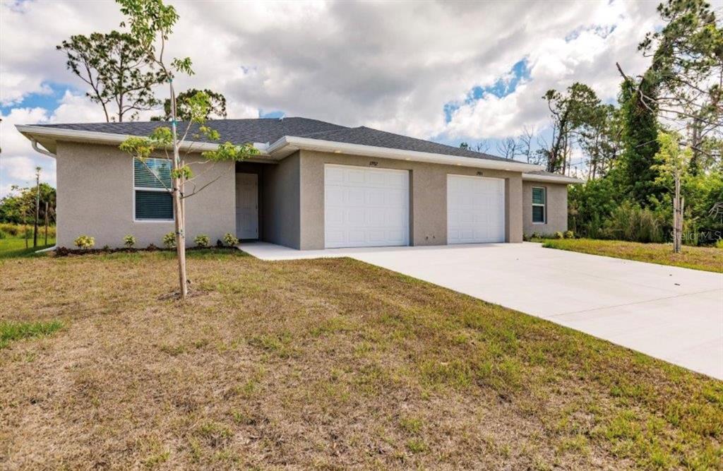 A single-story duplex with a gray stucco exterior, two garage doors, and a concrete driveway — 11982-11984 TETZEL AVENUE, PORT CHARLOTTE, FL
