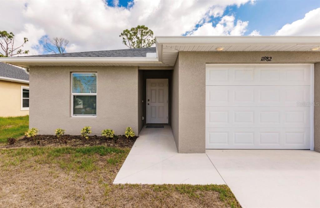 A single-story house exterior features a beige stucco facade, a white garage door, and a walkway — 11982-11984 TETZEL AVENUE, PORT CHARLOTTE, FL