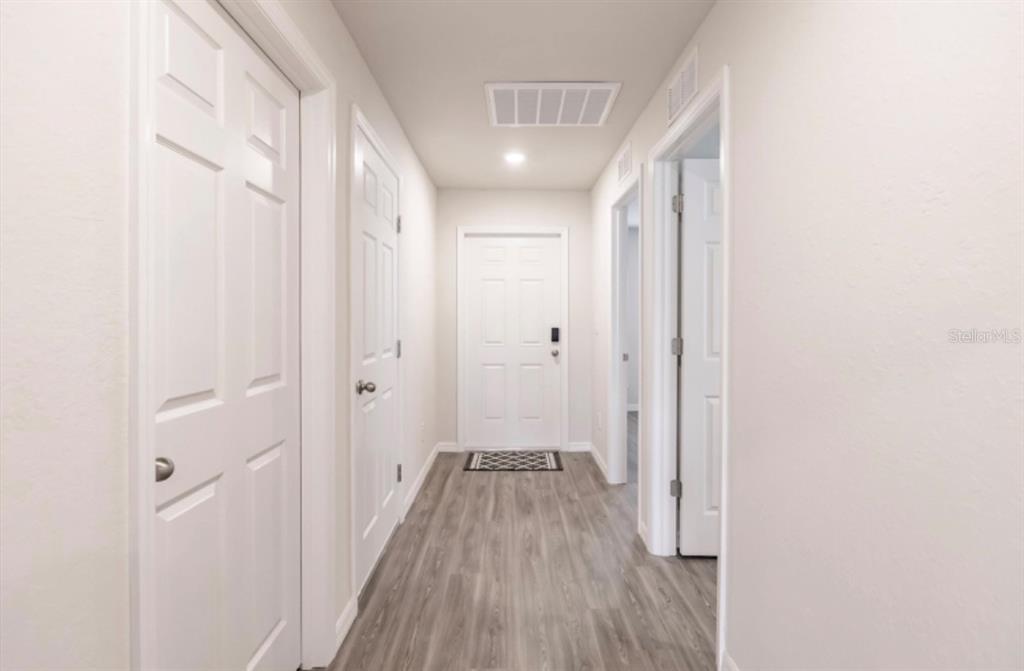 A hallway with light-colored walls, wood-look flooring, and several white interior doors — 11982-11984 TETZEL AVENUE, PORT CHARLOTTE, FL