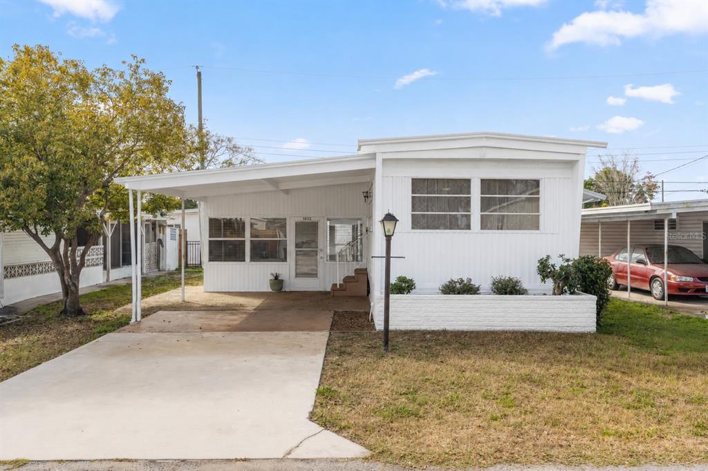 A white mobile home features a concrete driveway, a carport, and a small front garden — 1012 50TH AVE PLAZA W, BRADENTON, FL