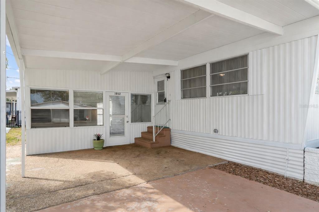 A covered carport area features a concrete floor, steps leading to a door, and windows — 1012 50TH AVE PLAZA W, BRADENTON, FL