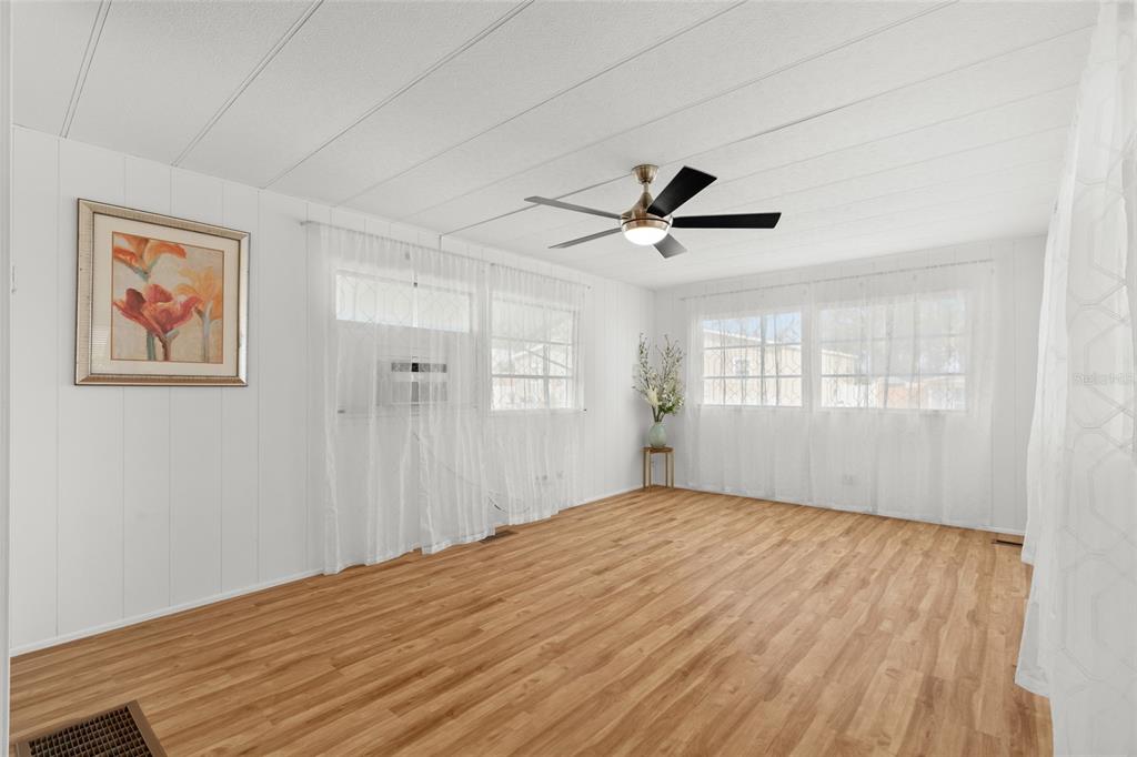A bright living room with white paneled walls, wood-look flooring, and a ceiling fan — 1012 50TH AVE PLAZA W, BRADENTON, FL