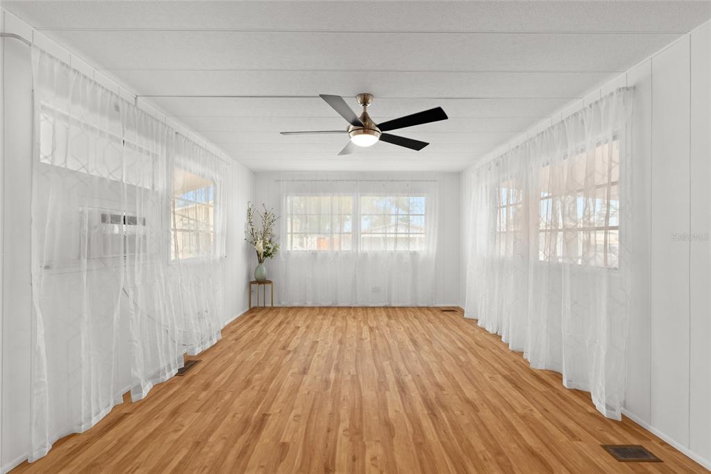 A sunroom with wood-look flooring, white walls, sheer curtains, and a ceiling fan — 1012 50TH AVE PLAZA W, BRADENTON, FL