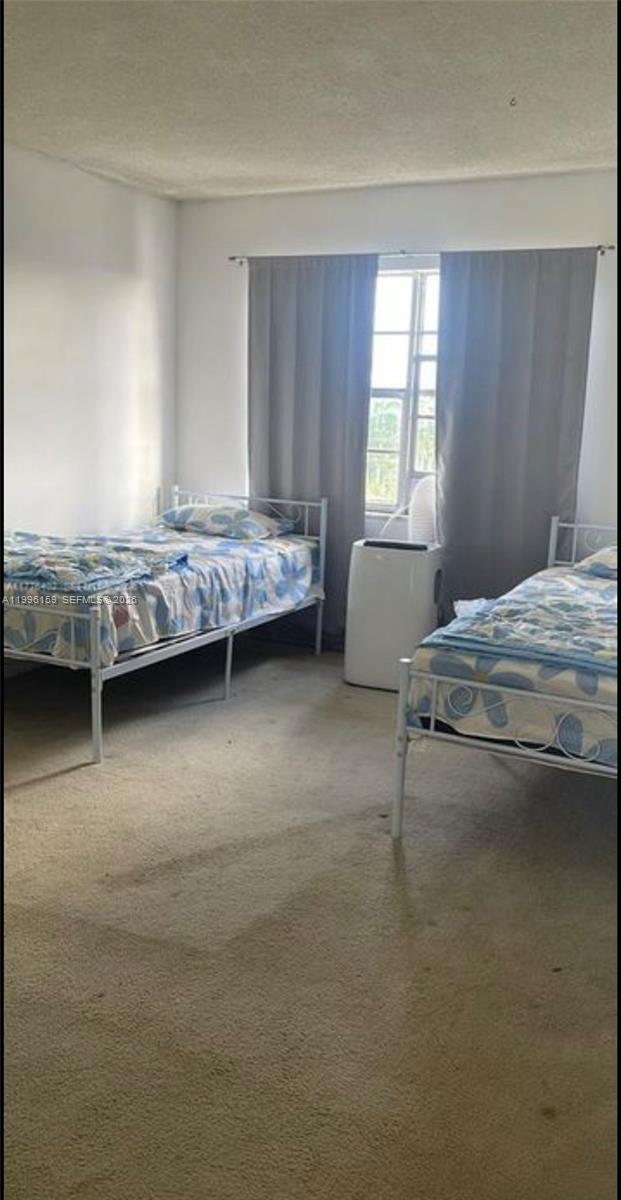 A bedroom features two twin beds with patterned bedding, beige carpeting, and a portable air conditioner — 496 NW 165th St Rd # 611, Miami FL 33169, MIAMI, FL