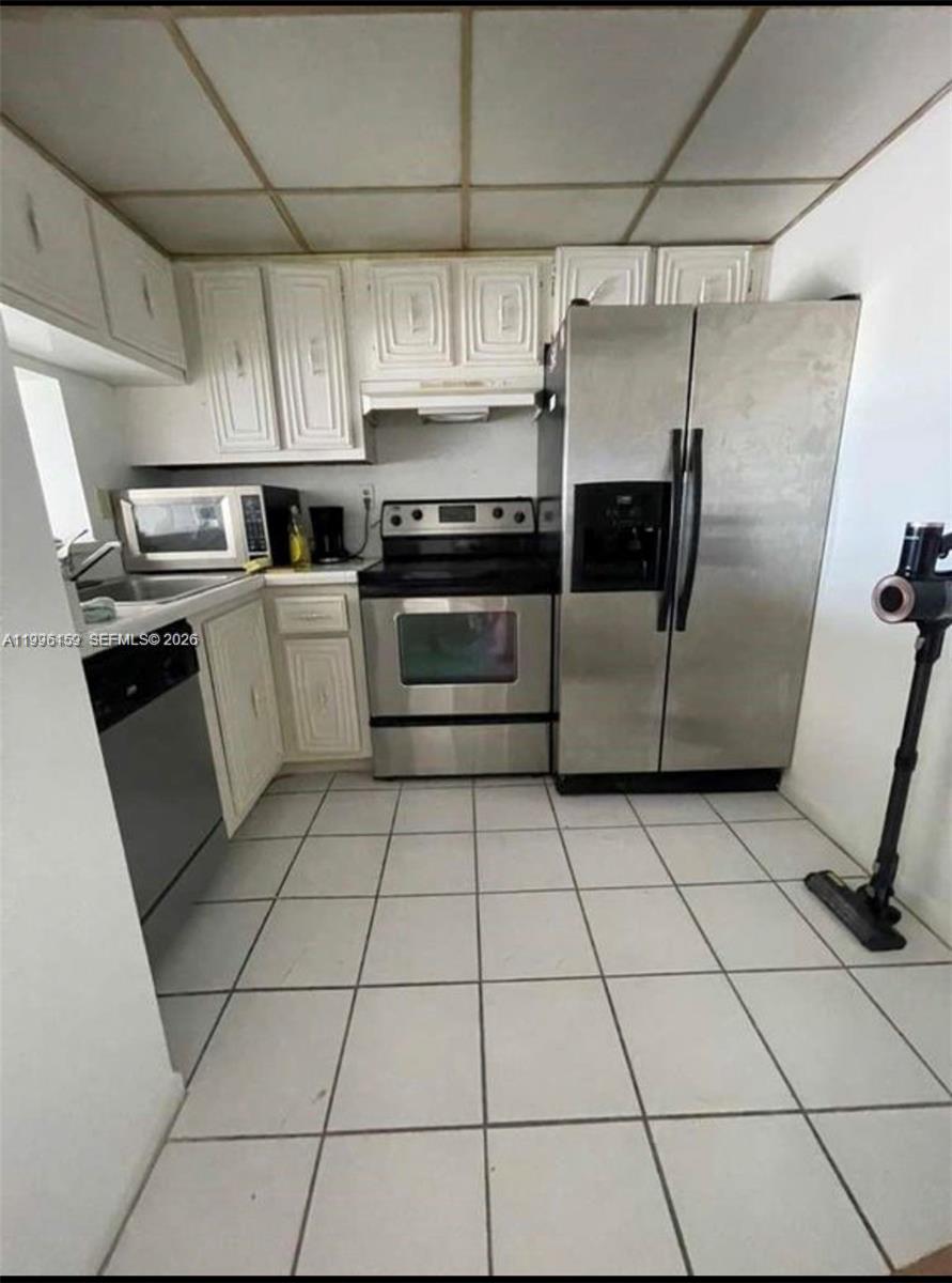 A kitchen with white cabinets, stainless steel appliances, and light-colored square floor tiles — 496 NW 165th St Rd # 611, Miami FL 33169, MIAMI, FL