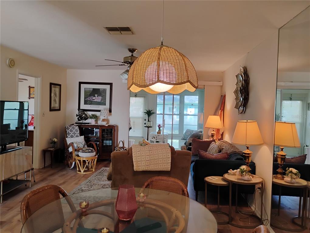 A living room and dining area feature a wicker pendant light, wood-look flooring, and mirrors — 2465 NORTHSIDE DRIVE UNIT 1001, CLEARWATER, FL