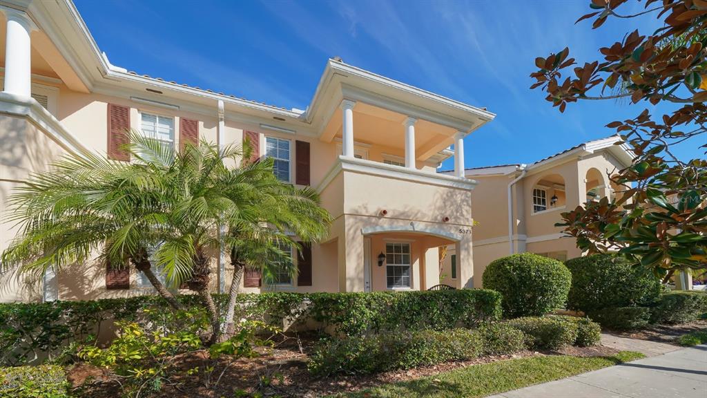 A two-story peach-colored townhouse with a palm tree, manicured hedges, and a covered entryway — 5373 DAVINI STREET, SARASOTA, FL
