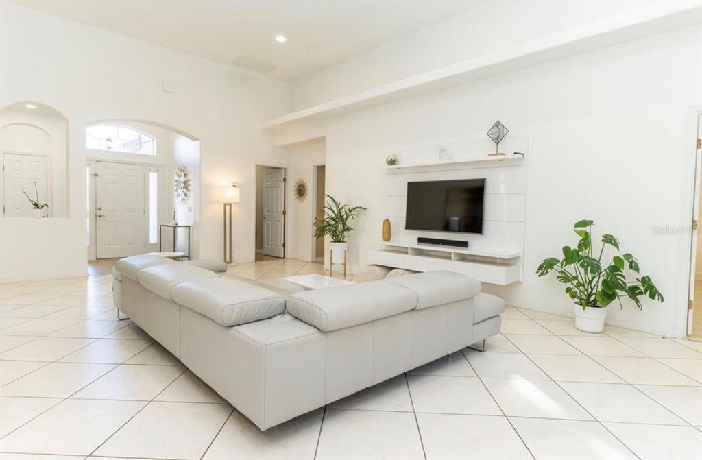 A spacious living room features white tile floors, a large sectional sofa, and a wall-mounted television — 2110 BUNKER VIEW COURT, KISSIMMEE, FL