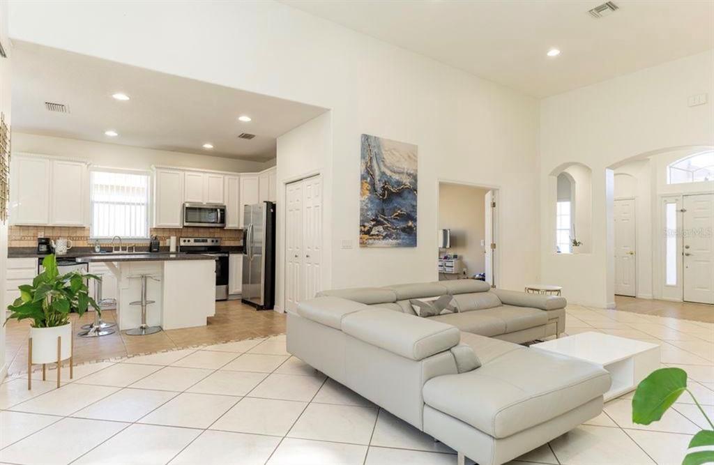 An open-concept living room with white tile floors, a grey sectional sofa, and a kitchen — 2110 BUNKER VIEW COURT, KISSIMMEE, FL