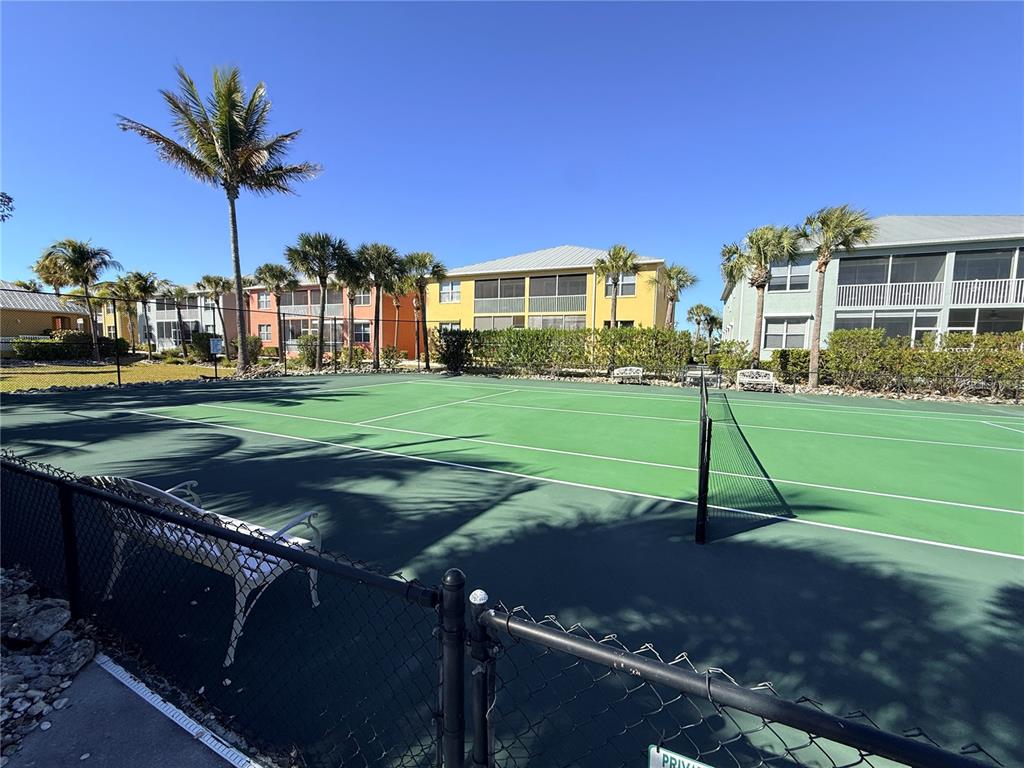 A tennis court with a chain-link fence and surrounding palm trees under a clear sky — 2002 BAL HARBOR BOULEVARD UNIT 1512, PUNTA GORDA, FL