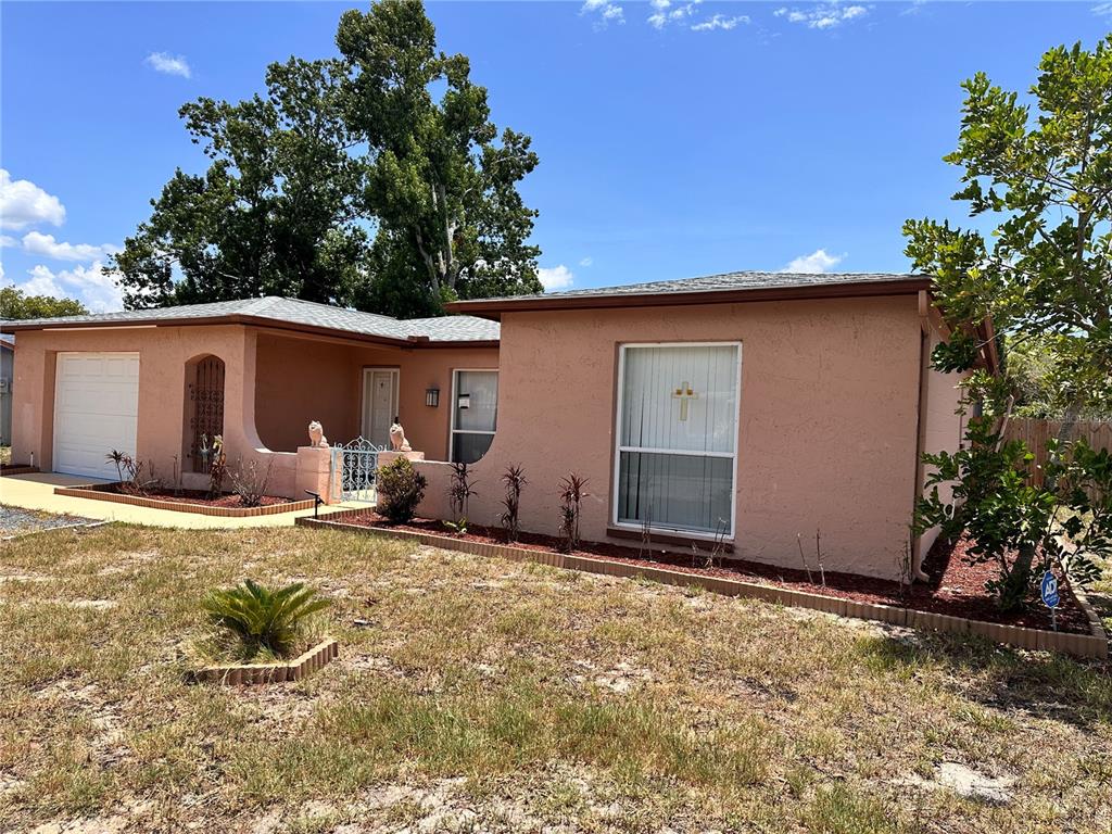 A single-story peach-colored house with a garage and a front yard under a blue sky — 7514 SAN MORITZ DRIVE, PORT RICHEY, FL