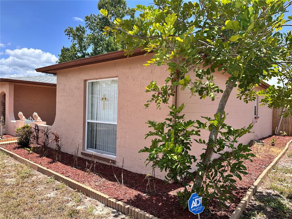 A peach-colored stucco house exterior features a window with a cross decoration and landscaping — 7514 SAN MORITZ DRIVE, PORT RICHEY, FL