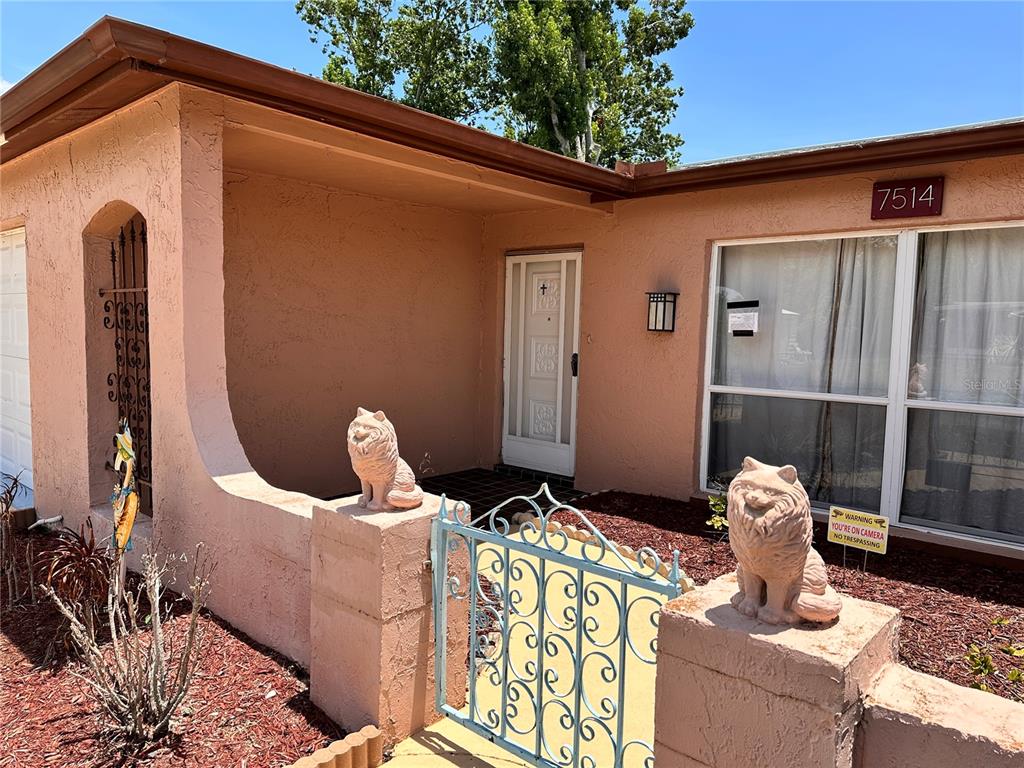 A peach-colored house exterior features a gated entryway with two cat statues and a window — 7514 SAN MORITZ DRIVE, PORT RICHEY, FL