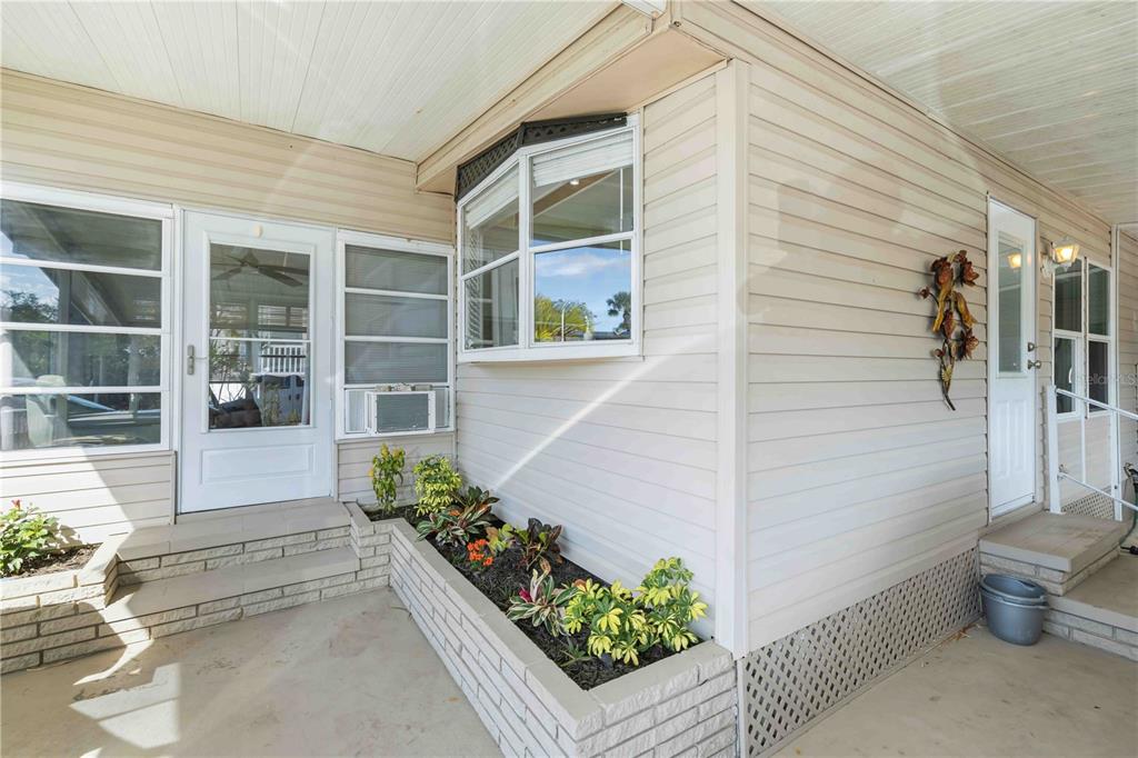 A beige vinyl-sided home exterior features a brick planter box and two white entry doors — 10303 BURNT STORE ROAD UNIT 54, PUNTA GORDA, FL
