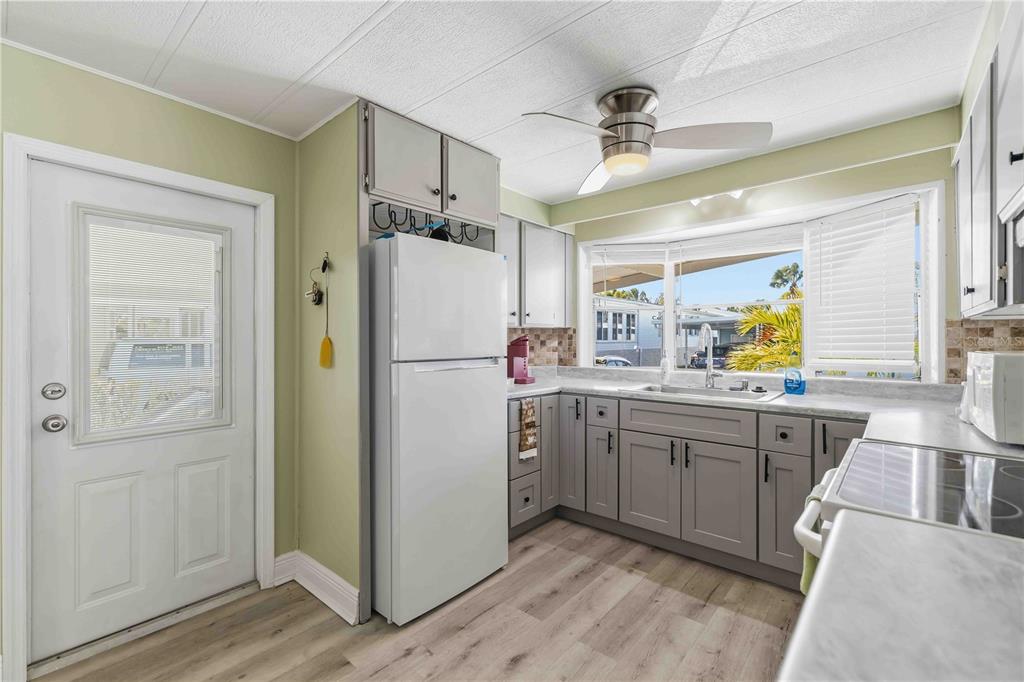 A kitchen features gray cabinets, a white refrigerator, light wood flooring, and a bay window — 10303 BURNT STORE ROAD UNIT 54, PUNTA GORDA, FL