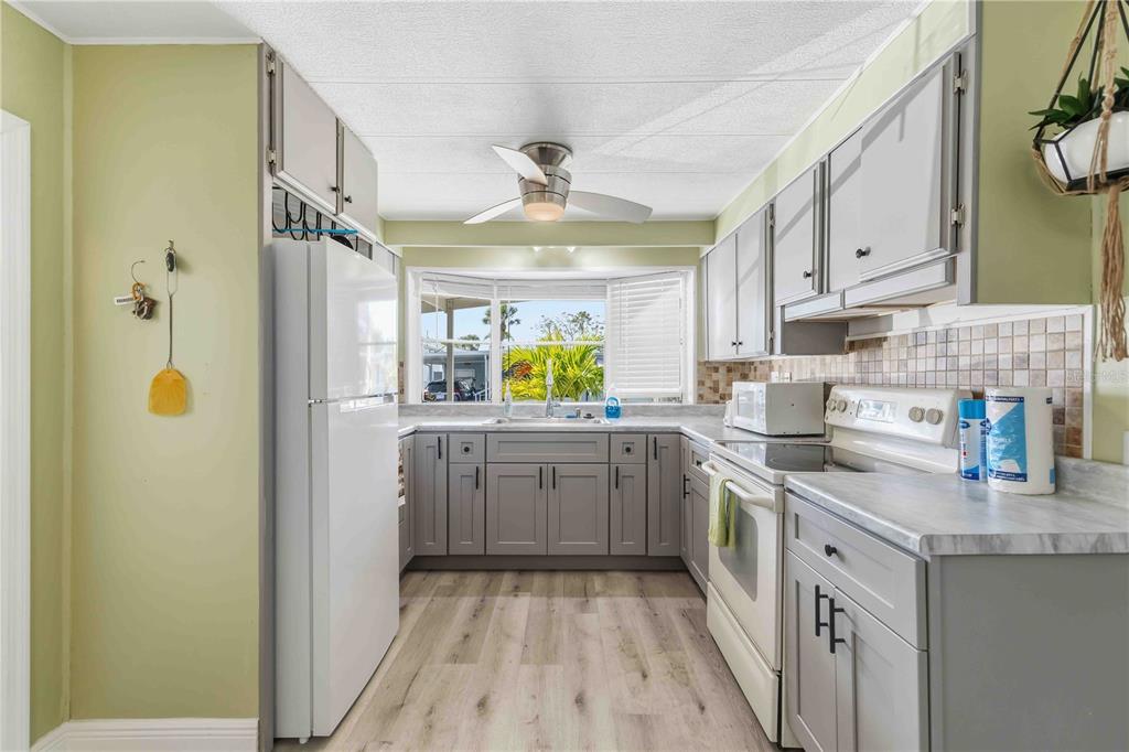 A kitchen with grey cabinets, white appliances, light wood-look flooring, and a window over the sink — 10303 BURNT STORE ROAD UNIT 54, PUNTA GORDA, FL