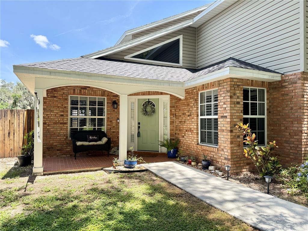 A brick house exterior features a covered front porch, a green door, and a walkway — 9306 ALANBROOKE ST, TEMPLE TERRACE, FL