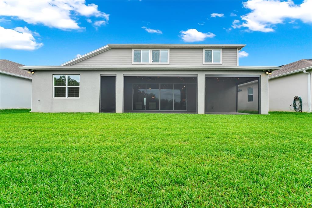 The rear exterior of a two-story house features a screened-in patio and a grassy yard — 2314 NUTHATCH STREET, ST CLOUD, FL