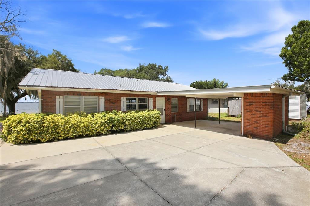 A single-story brick house features a metal roof, a concrete driveway, and an attached carport — 836 LAKE JUNE ROAD, LAKE PLACID, FL