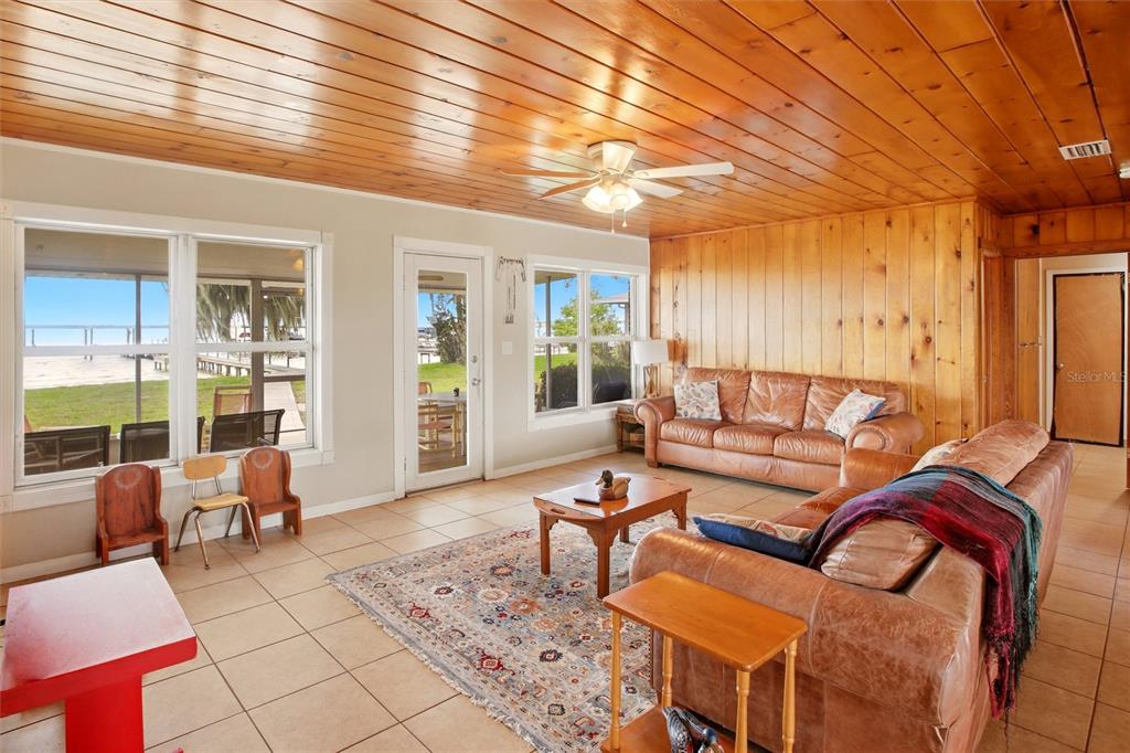 A living room features wood-paneled walls and ceilings, tile flooring, and large windows with water views — 836 LAKE JUNE ROAD, LAKE PLACID, FL