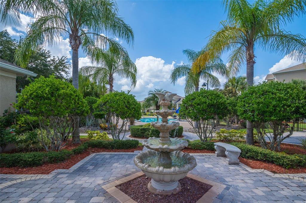 A tiered stone fountain sits on a paved patio surrounded by palm trees and landscaping — 6512 SWISSCO DRIVE UNIT 1417, ORLANDO, FL
